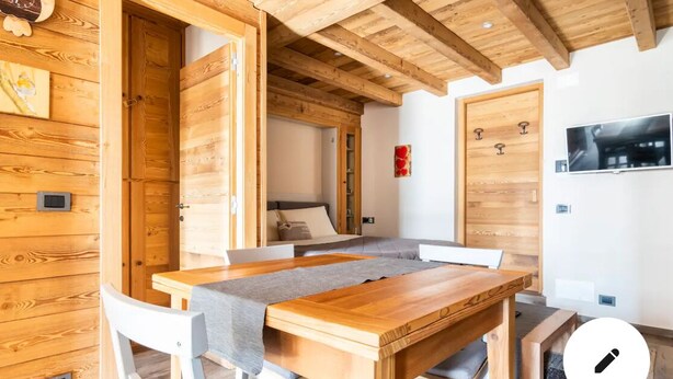 Une table à manger en bois, avec des chaises, un banc et un téléviseur fixé au mur.