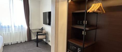 A hotel room with a bed, a desk, a television, a wardrobe, and a mirror.