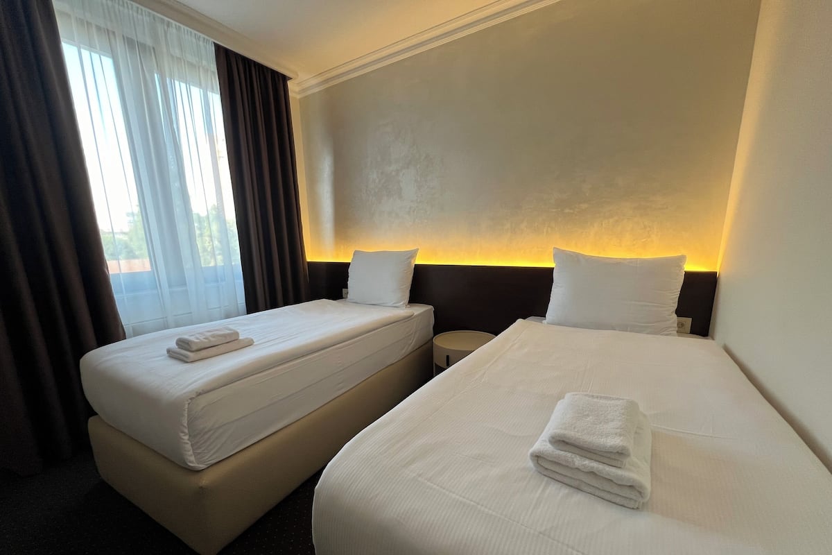Ein Hotelzimmer mit zwei Betten, einem Nachttisch und einem Fenster mit Vorhängen.