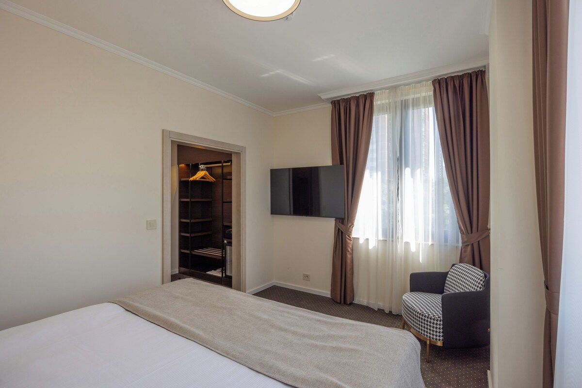 A hotel room with a bed, a TV mounted on the wall, a chair, and a wardrobe.