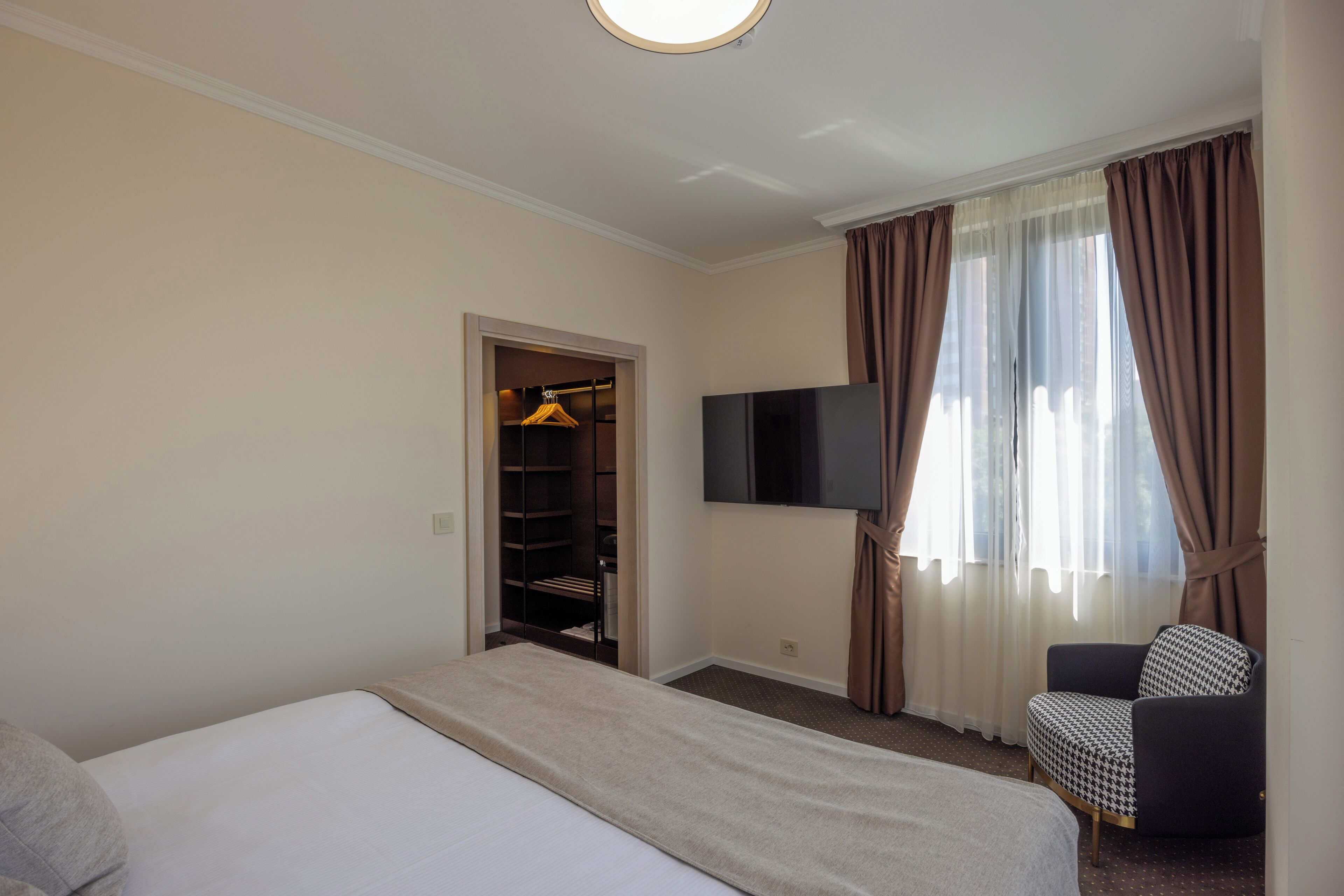 Ein Hotelzimmer mit Bett, Fernseher, Sessel und Kleiderschrank.