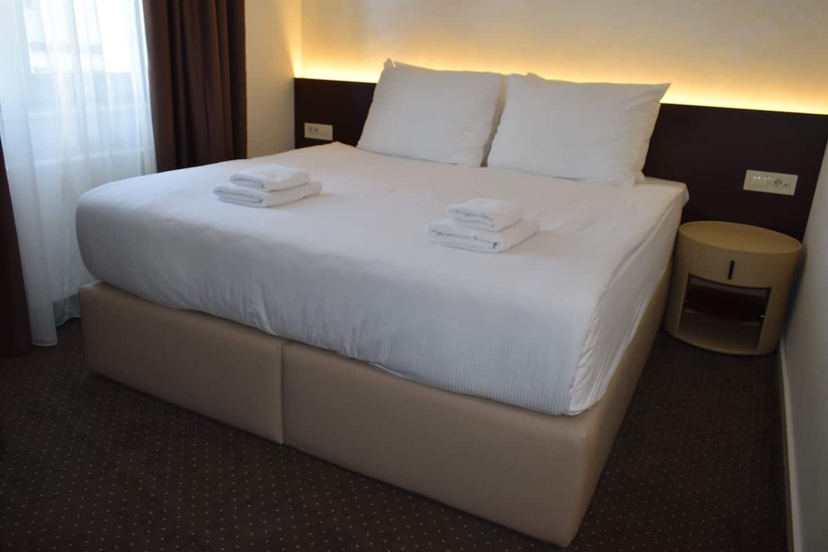 Ein Hotelzimmer mit einem großen Bett, zwei Kissen, einem Nachttisch und einem kleinen Hocker.