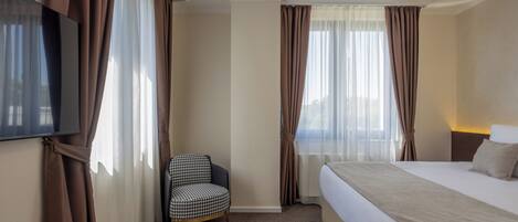 A hotel room with a bed, a chair, a television, and curtains.