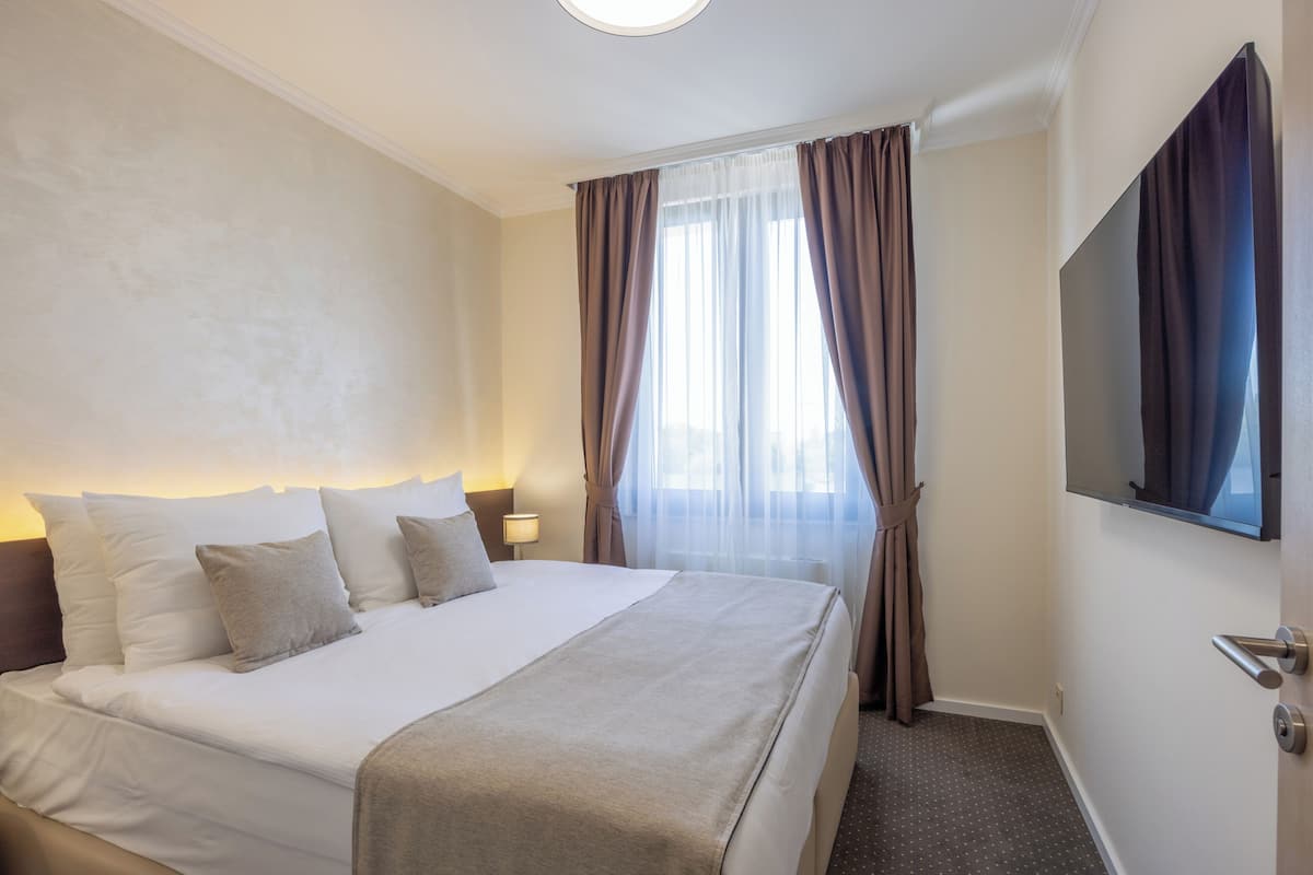 Ein Hotelzimmer mit einem großen Bett, einem Flachbildfernseher und einem Fenster mit Vorhängen.
