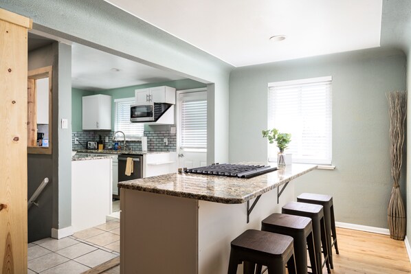 A modern kitchen with a central island, bar stools, and a view of the adjacent dining area.