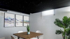 A conference room with a wooden table, white chairs, framed artwork on the wall, and a potted plant.