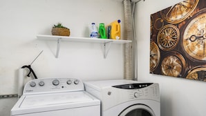 A laundry area with a Whirlpool washer and dryer, a shelf with cleaning supplies, and a wall-mounted compass decoration.