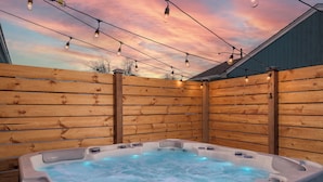 Un bain à remous entouré d’une clôture en bois et illuminé de guirlandes lumineuses.