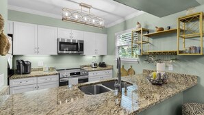 A modern kitchen with white cabinets, a stainless steel microwave, a built-in oven, granite countertops, a sink, and a hanging light fixture. - MIDDLE OF 30A! MINUTES FROM BEACH, POOLS, TENNIS COURTS and NATURE TRAILS! (Santa Rosa Beach)