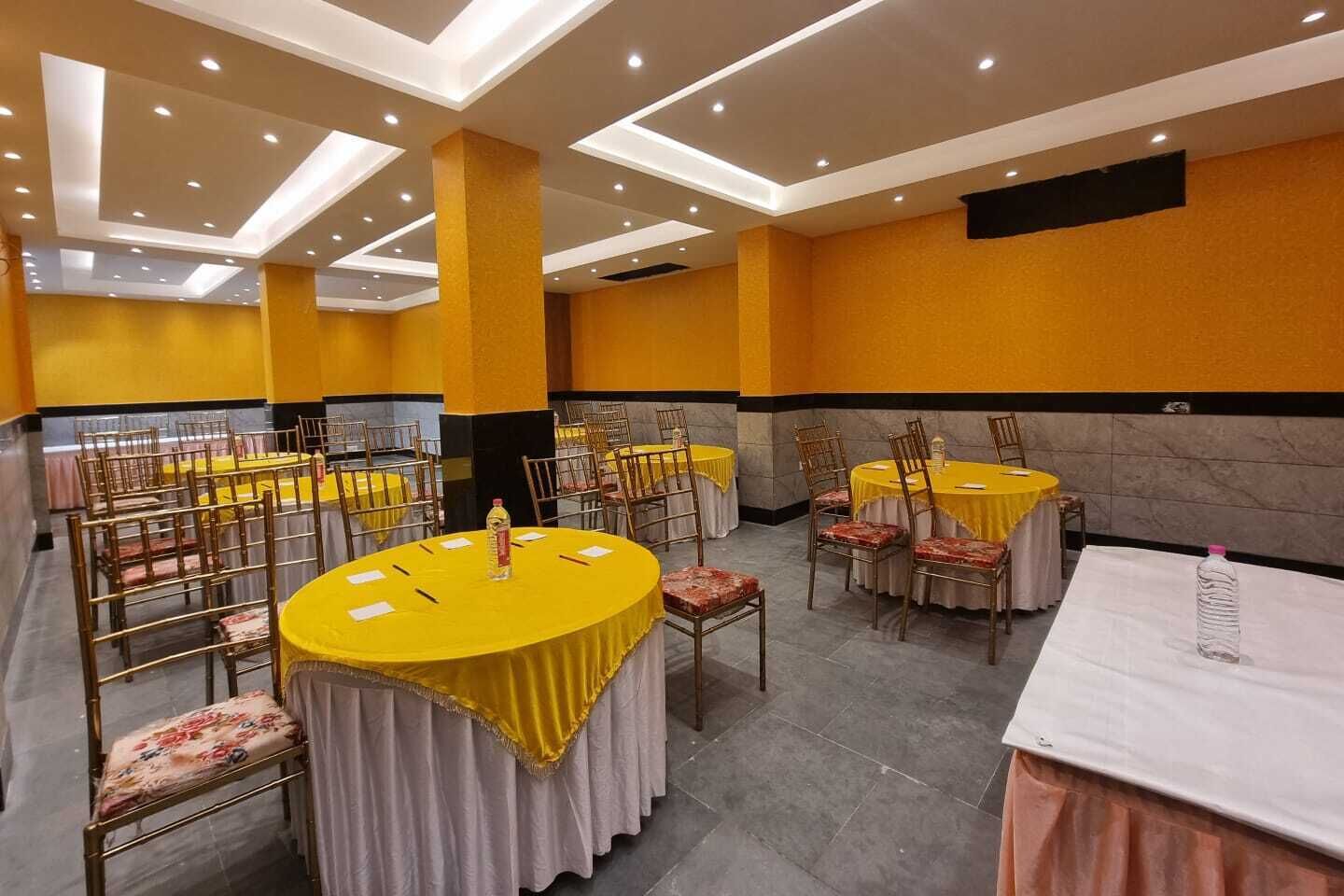 A banquet hall with round tables covered in yellow tablecloths, arranged in rows with chairs.