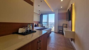 Moderni hotellihuone, jossa on pieni keittiönurkkaus, sängystä avautuva kaunis näkymä ja seinälle asennettu taulutelevisio.