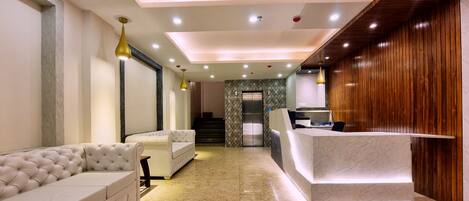 A modern hotel lobby with a reception desk, plush seating, and a staircase leading to an elevator.