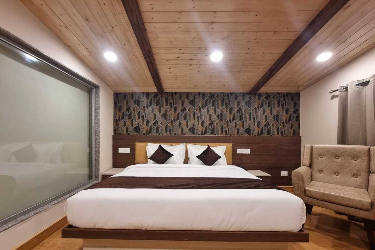 A bedroom with a large bed, a wooden headboard, a chair, and a view of a cityscape.