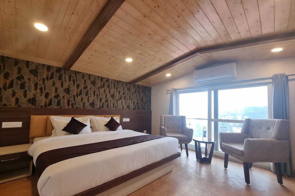 A hotel room with a large bed, two armchairs, a small table, and a window with a view.