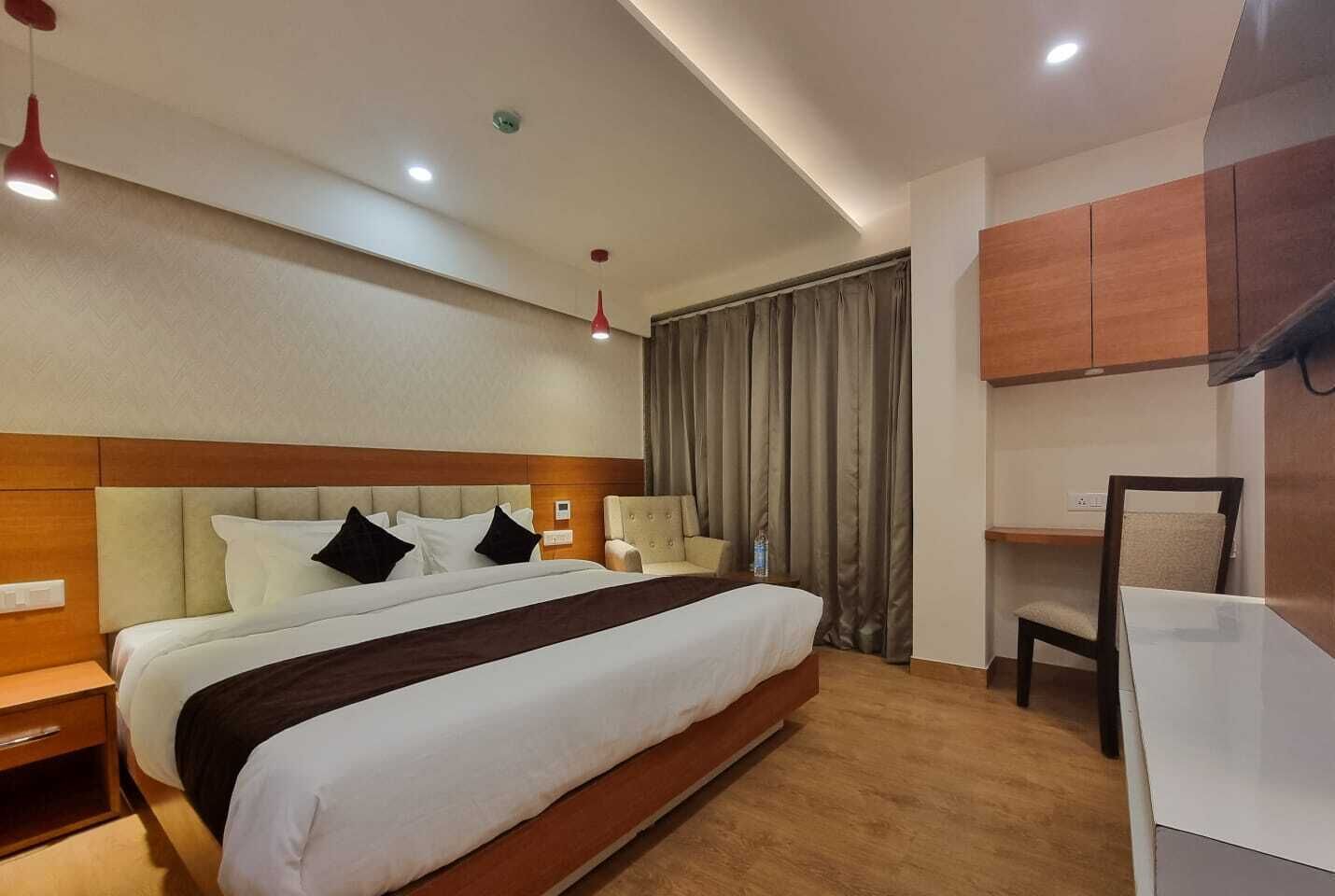 A hotel room with a large bed, a desk, a chair, and a wardrobe.