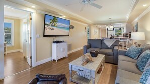 A spacious living room with a large flat-screen TV, a ceiling fan, and a cozy seating area with a sofa and a coffee table. - Beachfront, Breathtaking Gulfviews with Resort Pool and Spectacular Sunsets. (HOLMES BEACH)