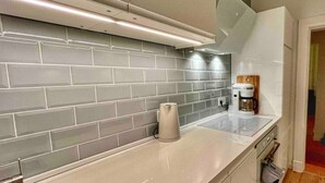 A modern kitchen with grey tiled backsplash, a coffee machine, and a kettle on the counter. - Ferienwohnung Burghof 3 + Balkon + Radparkplatz (Flensburg)