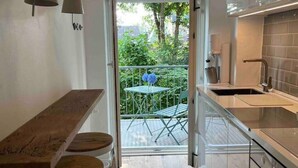 A compact kitchen with a dining area, a balcony with a table and chairs, and a view of greenery outside. - Ferienwohnung Burghof 3 + Balkon + Radparkplatz (Flensburg)