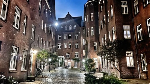 A cobblestone street lined with brick buildings, featuring a central archway and a bicycle parked in front. - Ferienwohnung Burghof 3 + Balkon + Radparkplatz (Flensburg)
