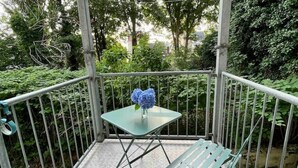 A balcony with a metal railing, a small table with a vase of flowers, and a green bench. - Ferienwohnung Burghof 3 + Balkon + Radparkplatz (Flensburg)