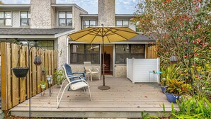 Un patio cubierto con mobiliario exterior, una sombrilla amarilla y una terraza de madera.