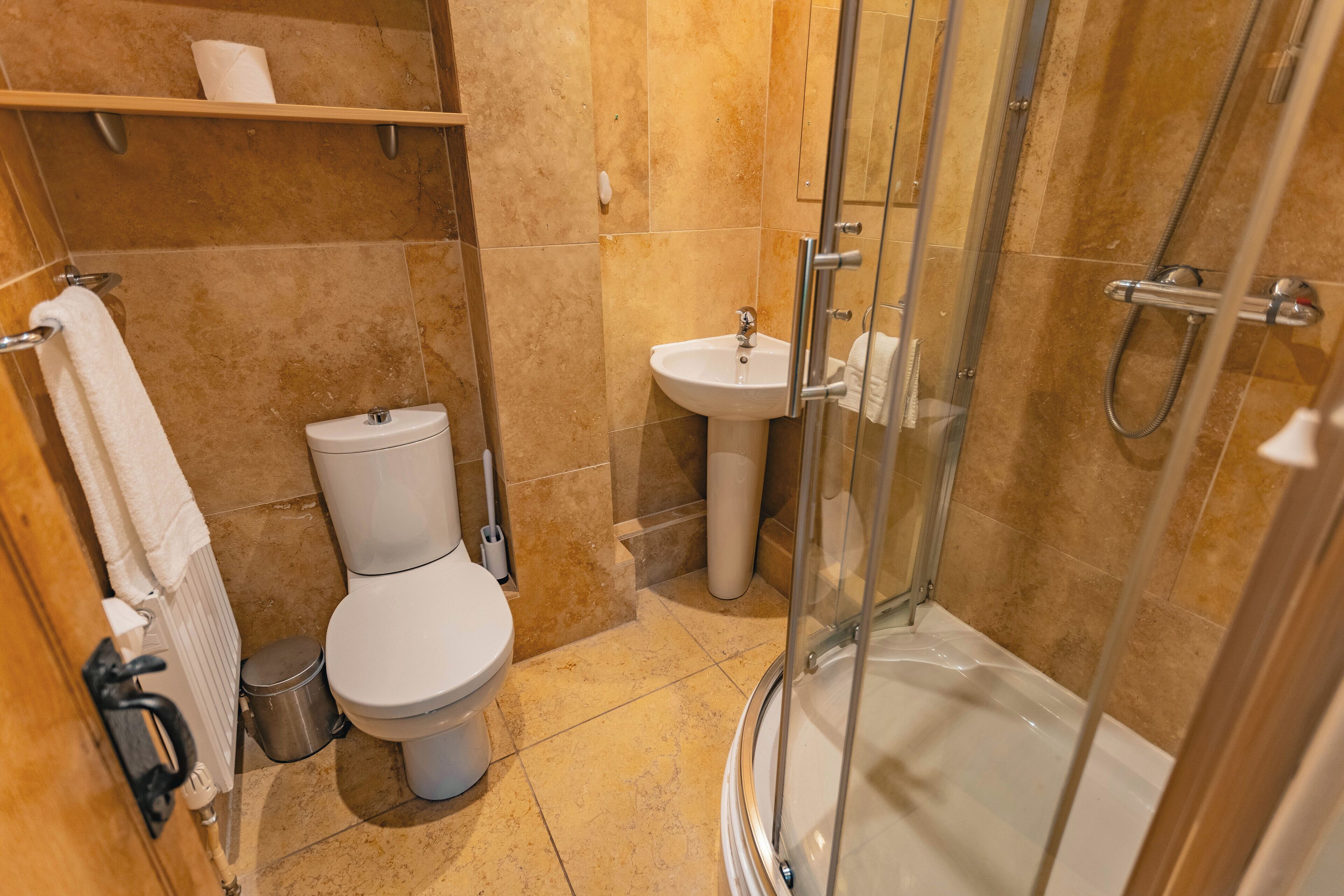 Un baño con inodoro, lavamanos y ducha con mampara de vidrio.