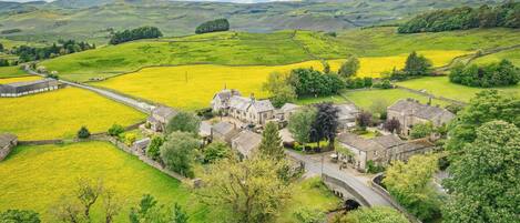 A rural village with stone buildings, a river, and fields of yellow flowers.