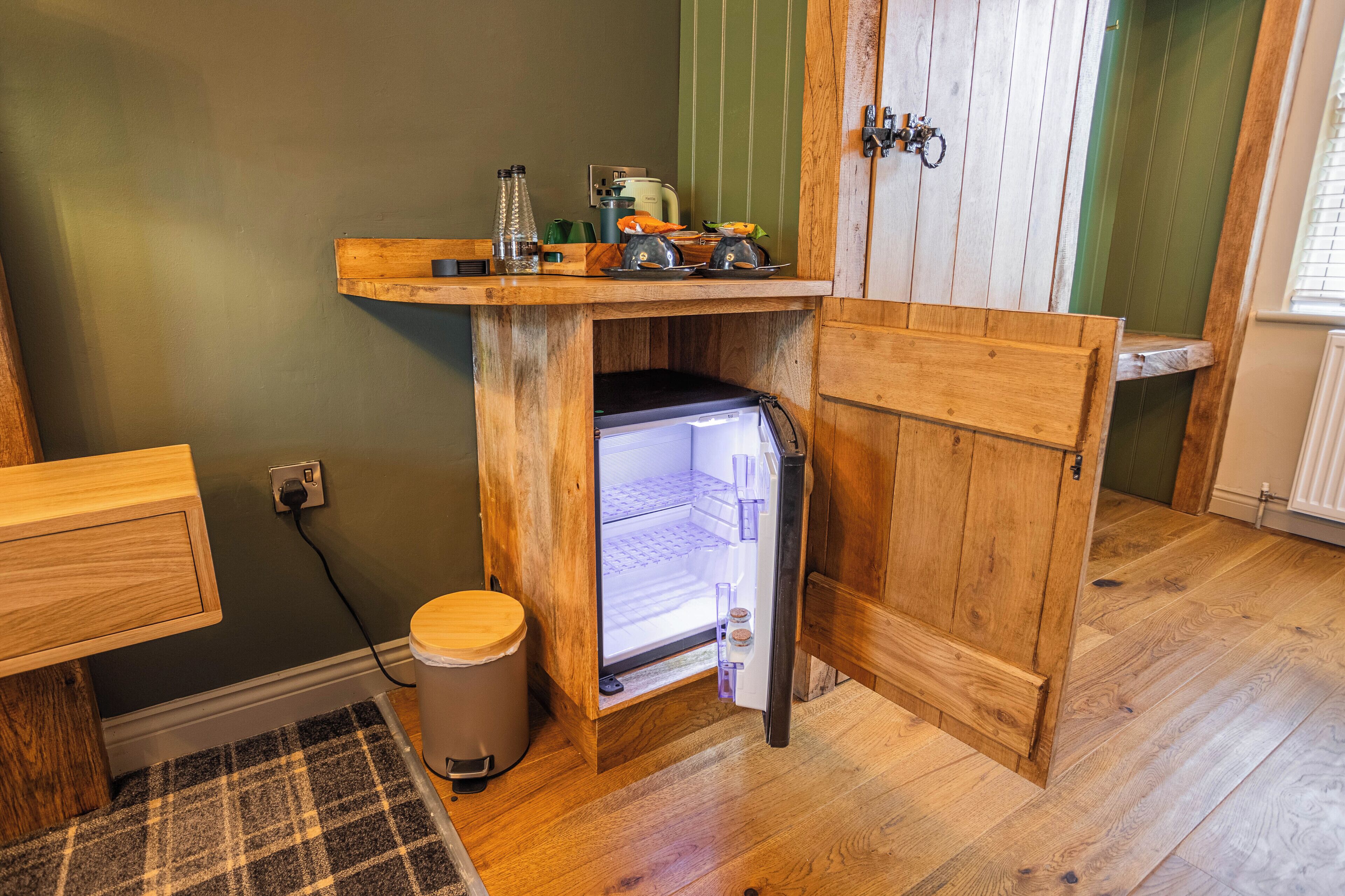 A compact kitchen with a built-in refrigerator, wooden countertop, and a small trash bin.
