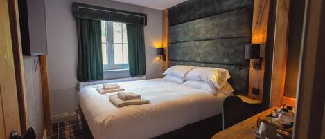 Een hotelkamer met een groot bed, een houten hoofdeinde, een nachtkastje met een lamp en een raam met gordijnen.