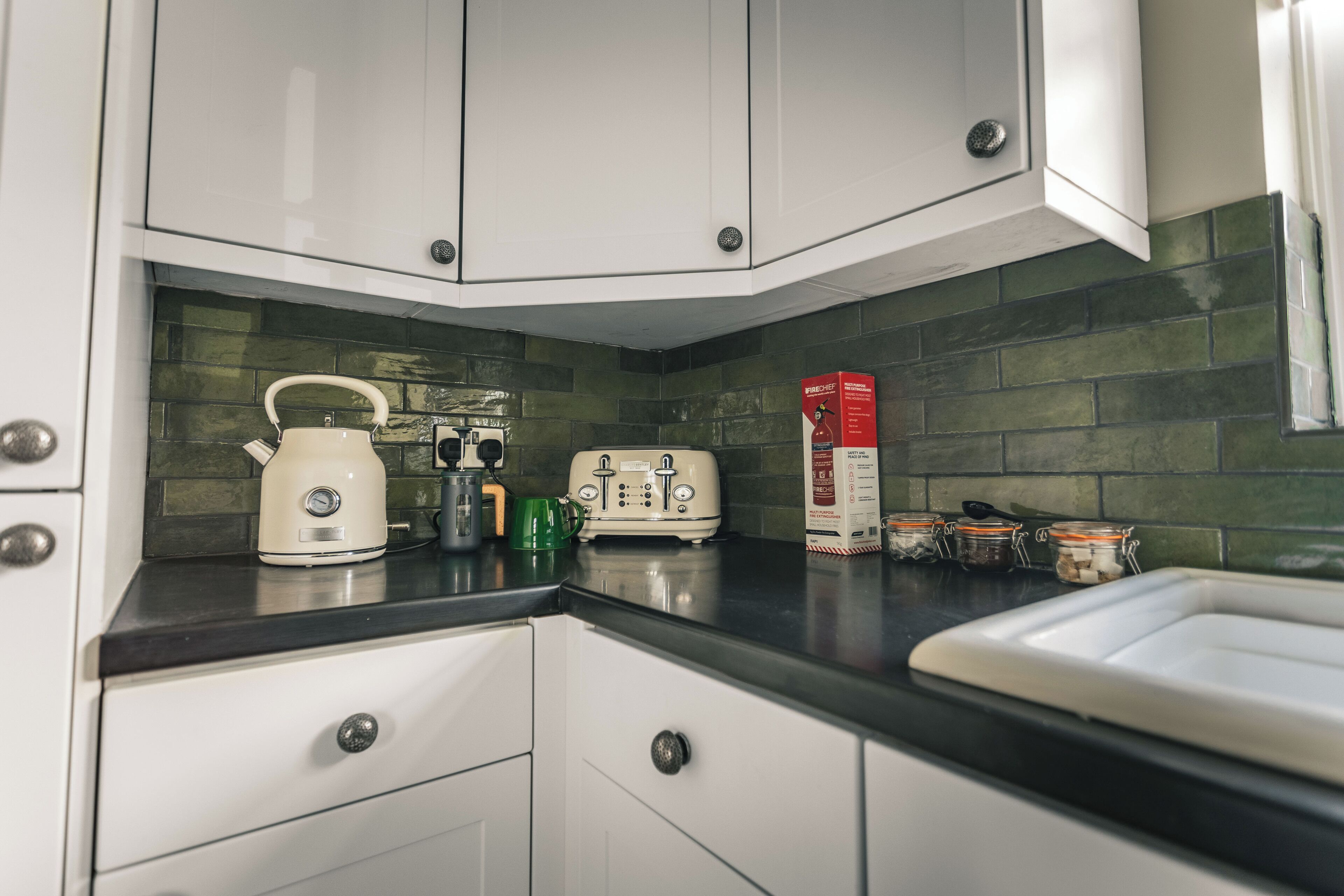 A kitchen with white cabinets, a black countertop, a kettle, a toaster, and a box of cereal.