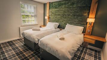 A hotel room with two beds, a window with blinds, a radiator, and a plaid carpet.