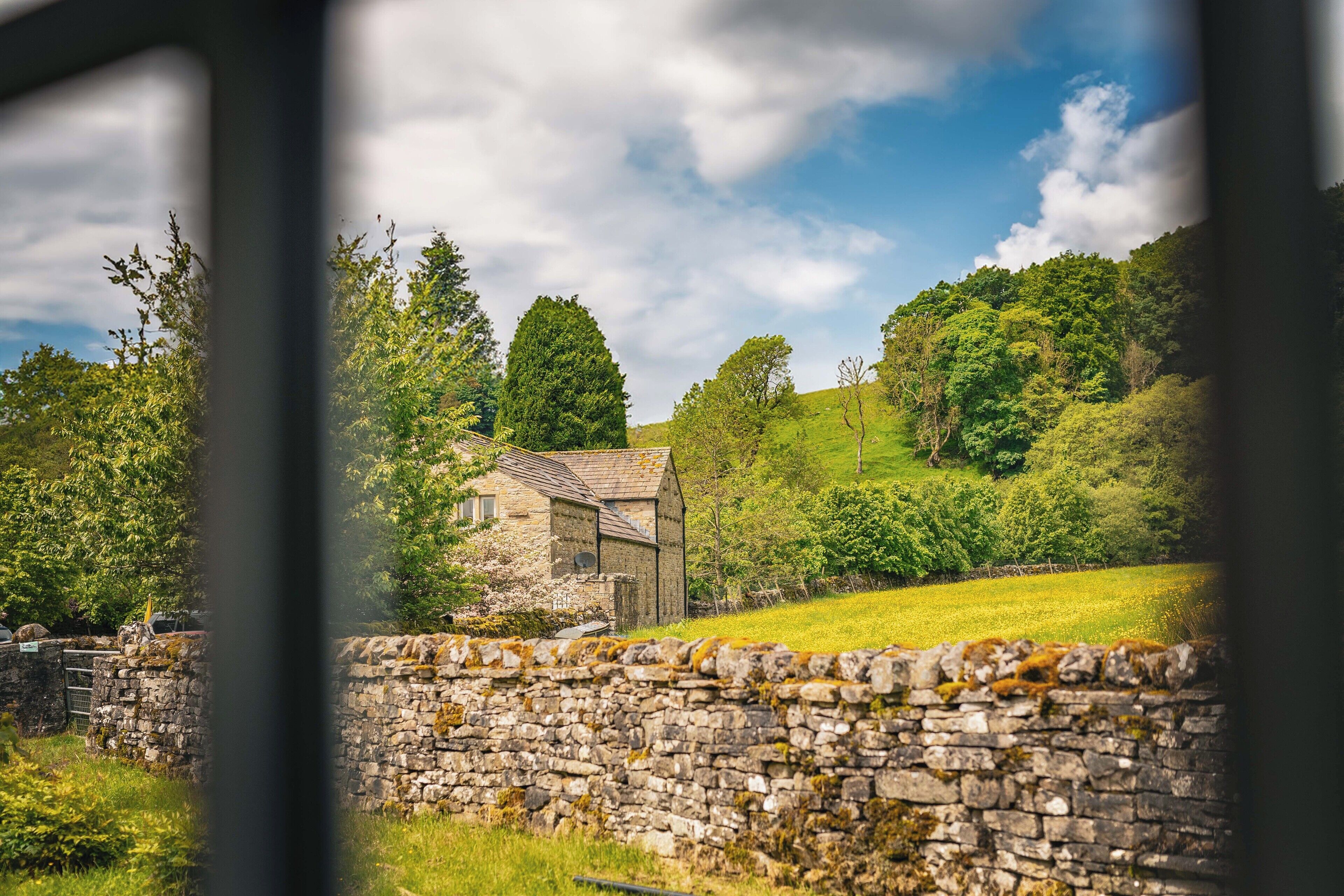 A stone wall and a stone building with a sloped roof, surrounded by lush greenery and trees.