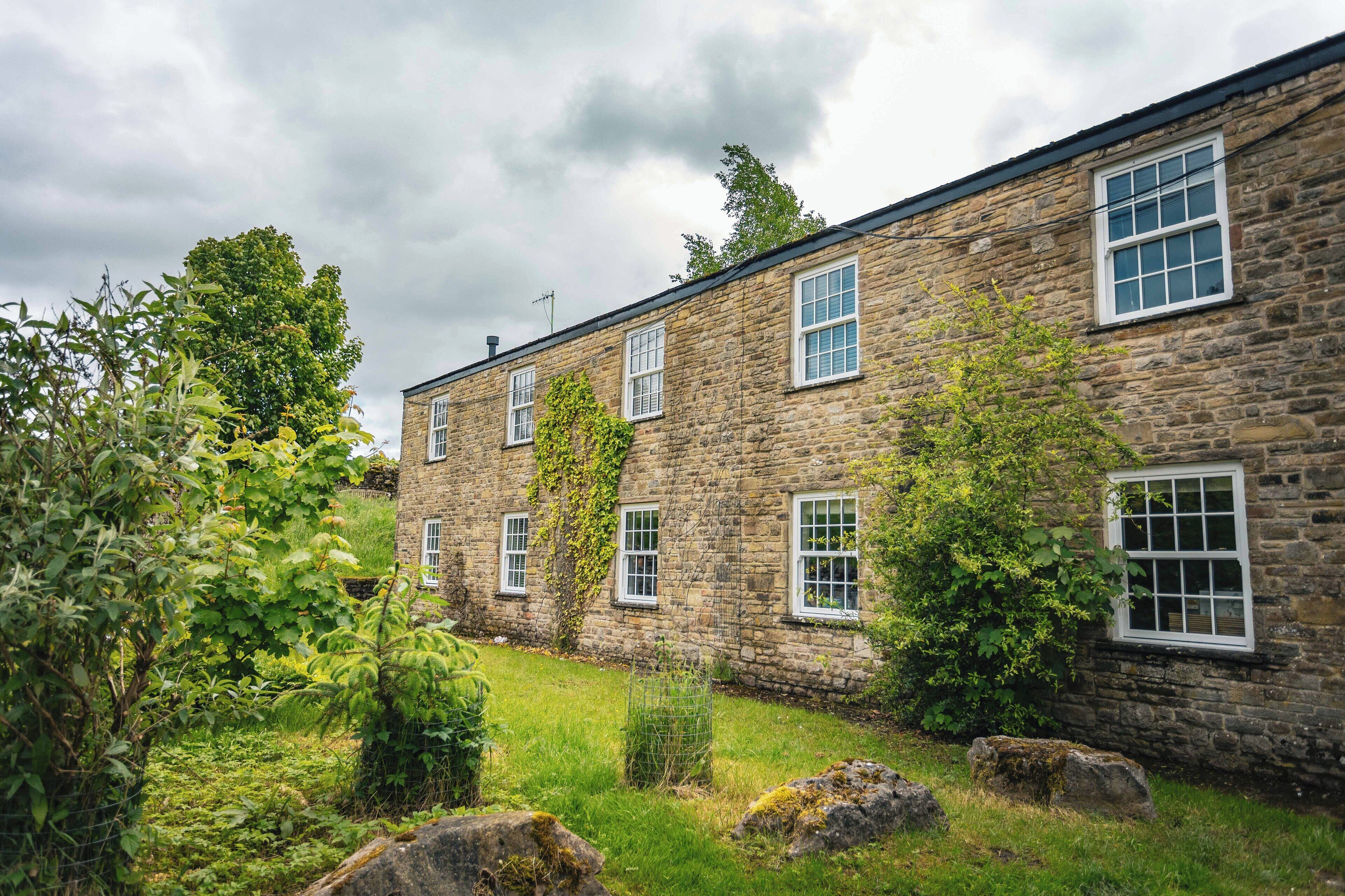 A stone building with multiple windows and a garden area with grass and rocks.