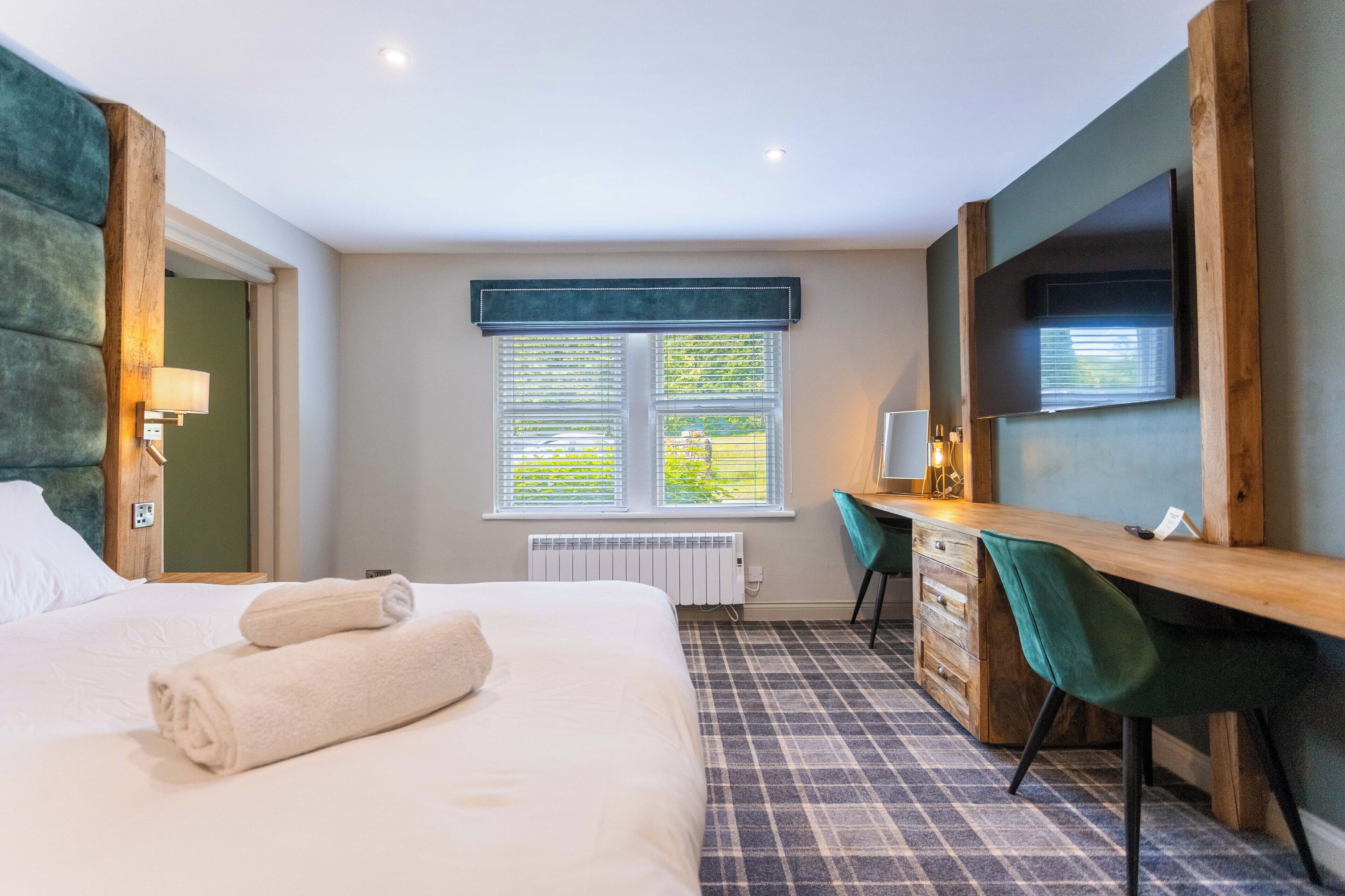 Une chambre d’hôtel avec un lit, un bureau, une chaise et une grande fenêtre avec des stores.