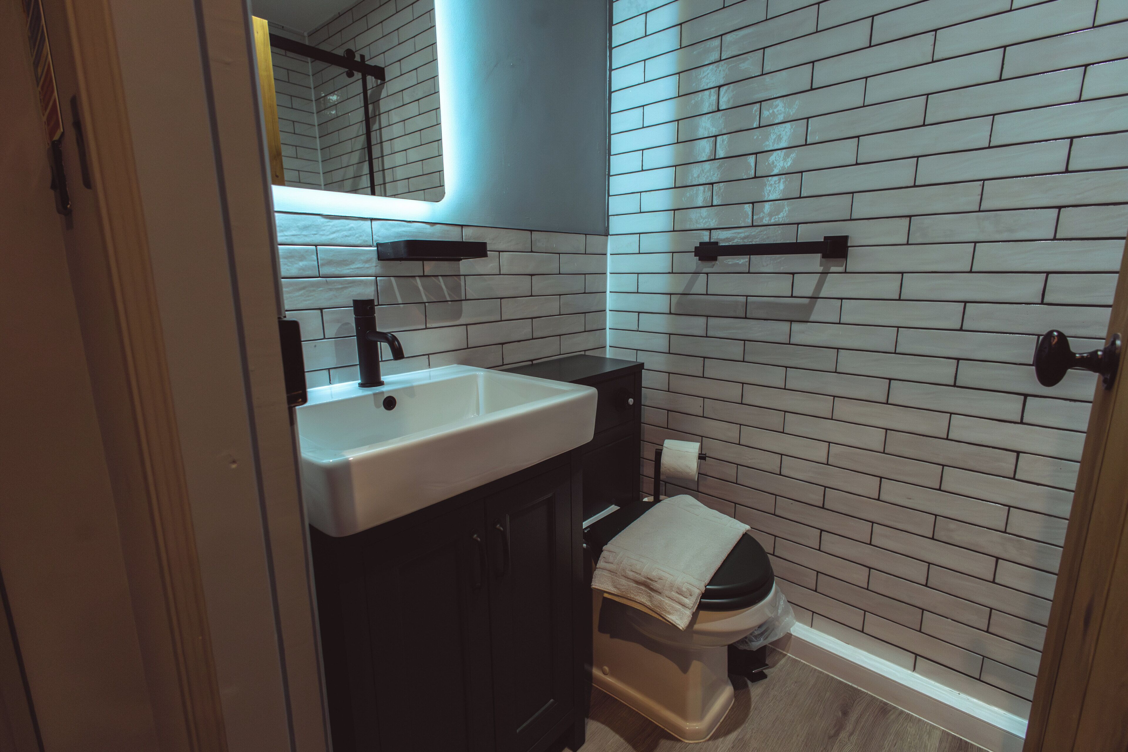 Une salle de bain avec un lavabo blanc, un meuble noir et des toilettes sur lesquelles est posée une serviette.