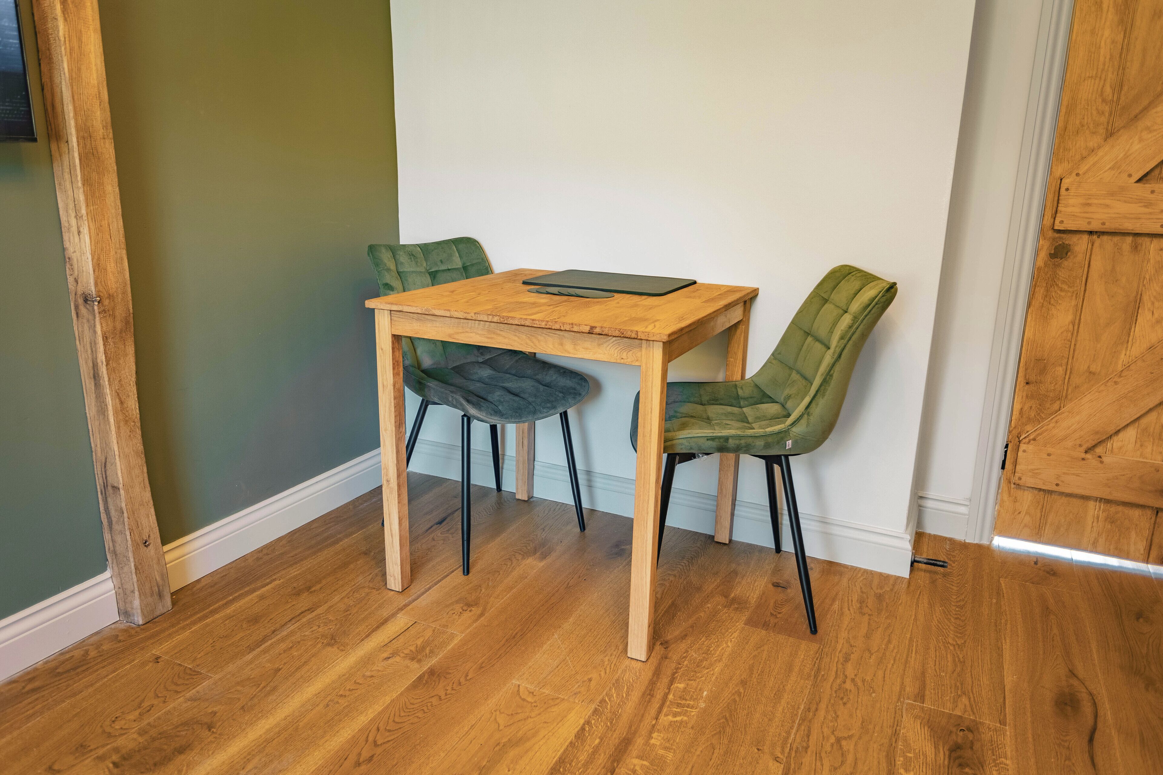Un pequeño comedor con una mesa de madera y dos sillas tapizadas en verde.
