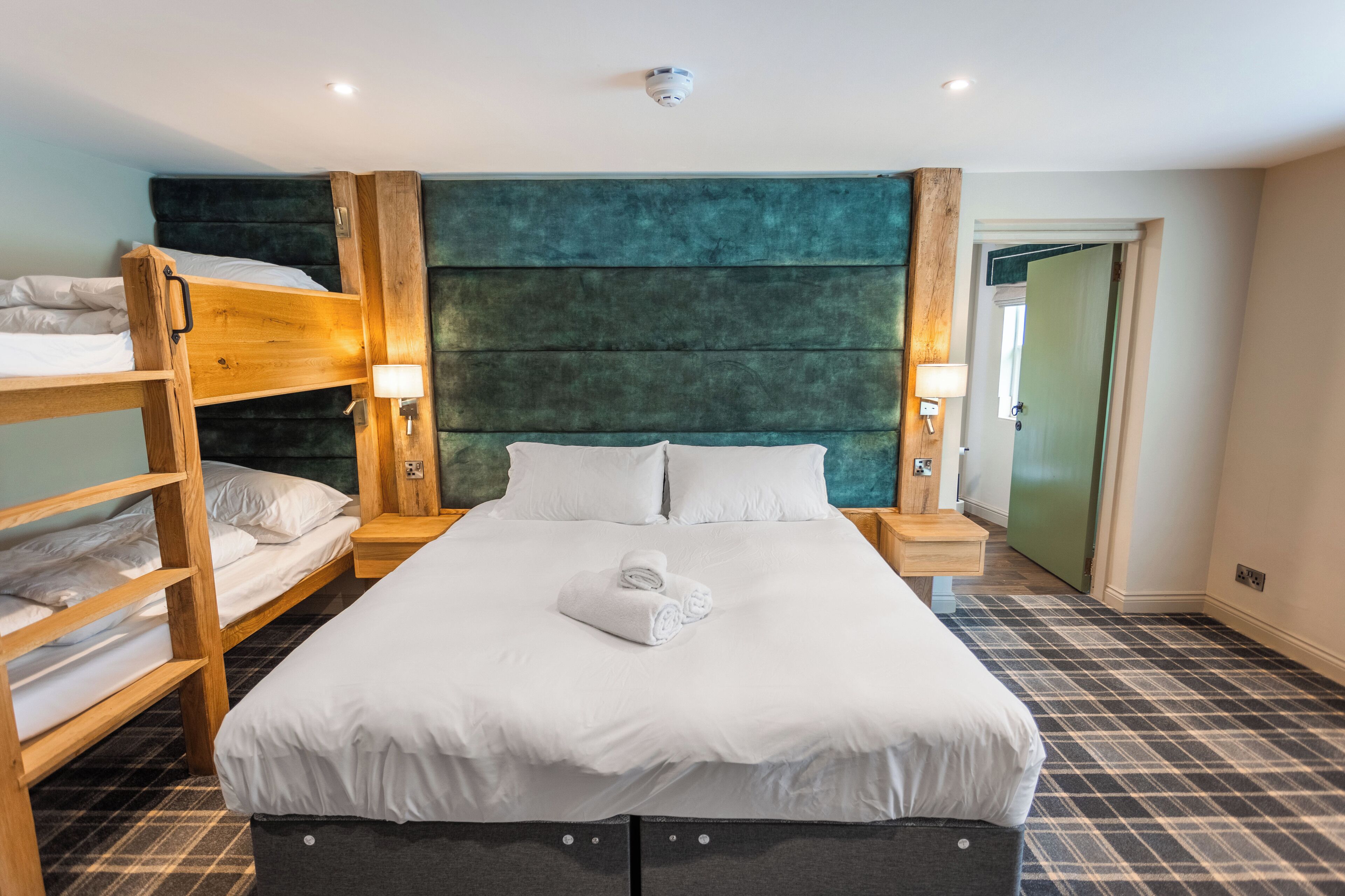 Ett hotellrum med en stor säng, två sängbord, en våningssäng och en vägg som är målad i en accentfärg – grönt.