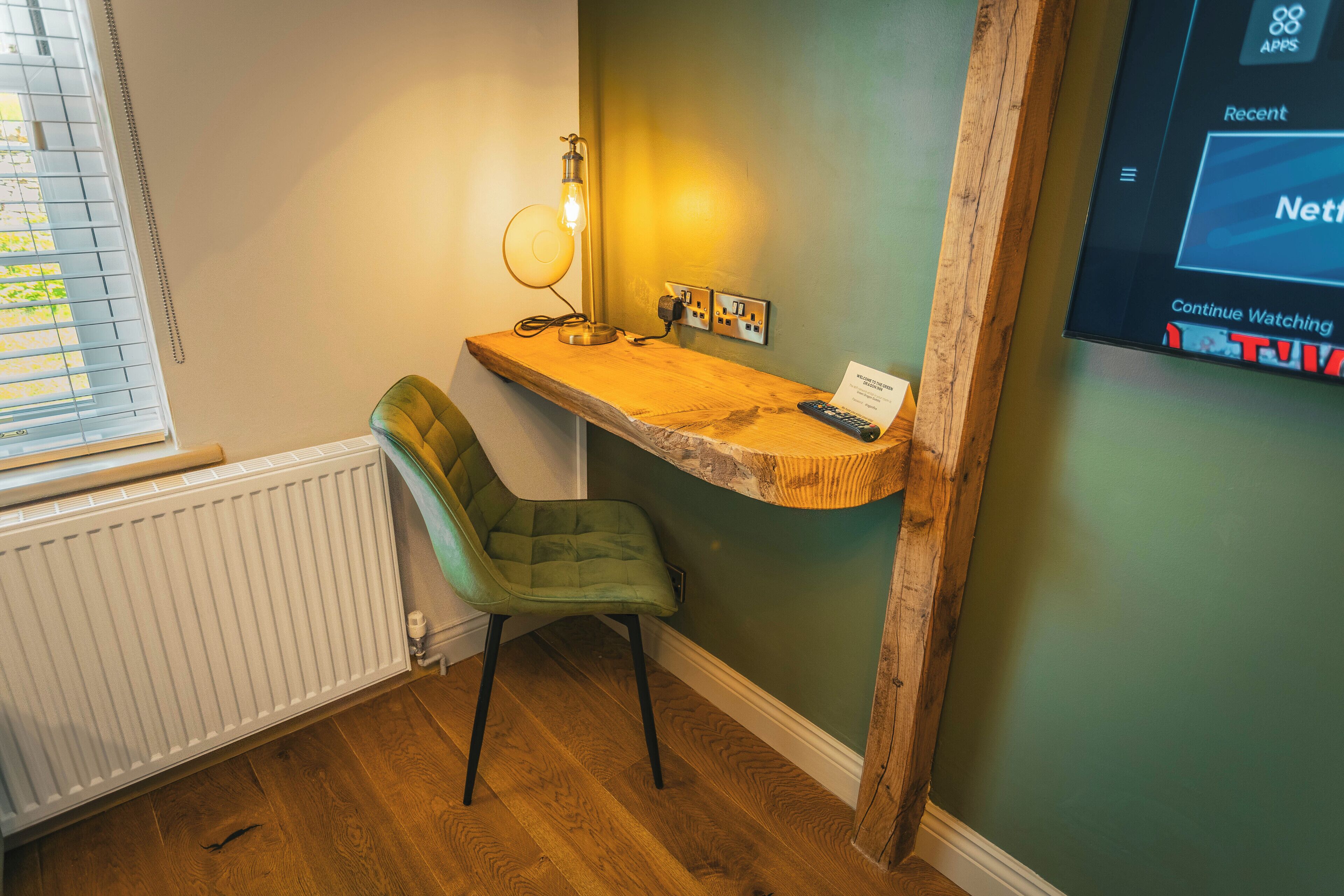 Una habitación con un escritorio de madera, una silla verde, un radiador y un televisor de pared mostrando la interfaz de Netflix.
