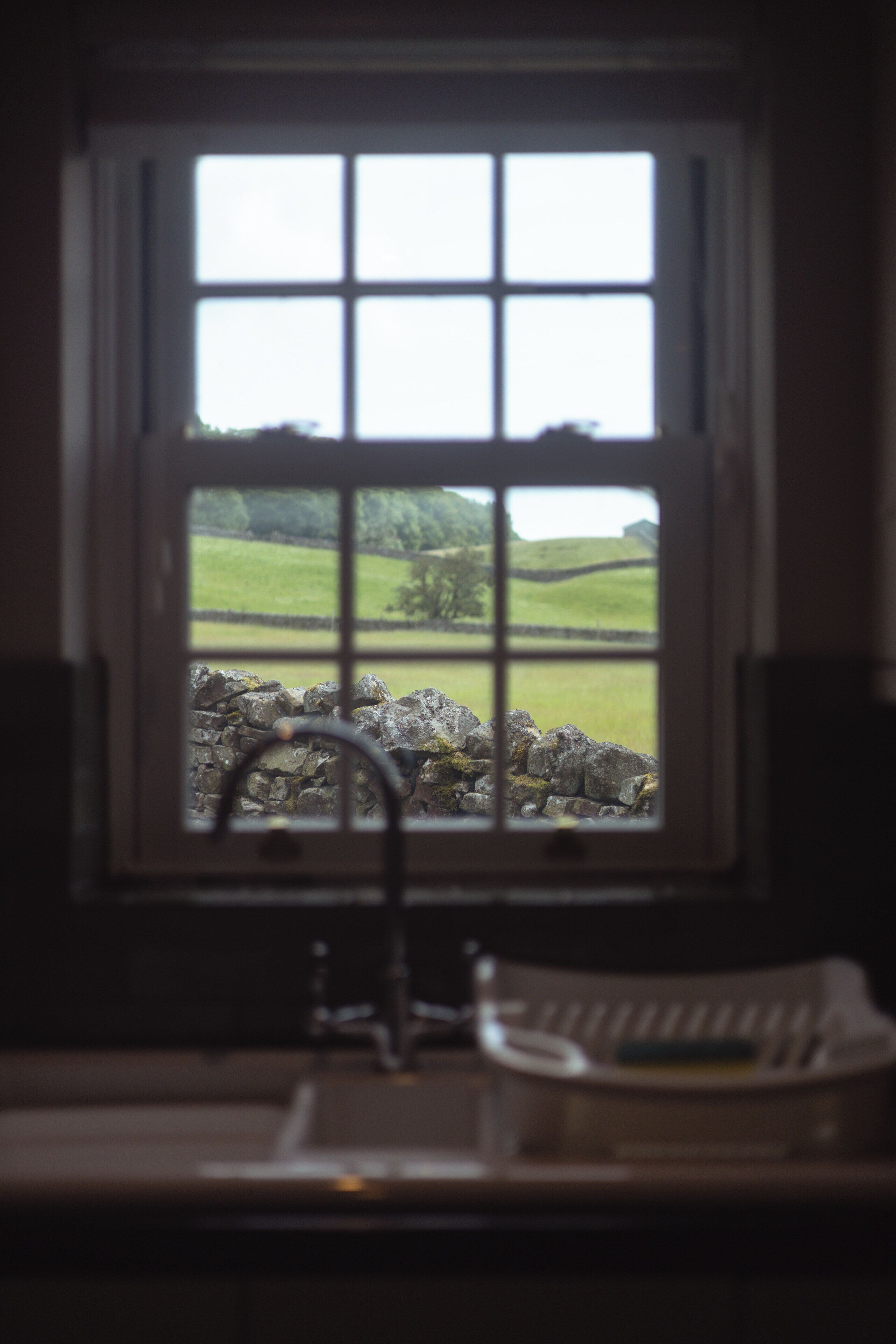Una ventana con vistas a un muro de piedra y campos verdes.
