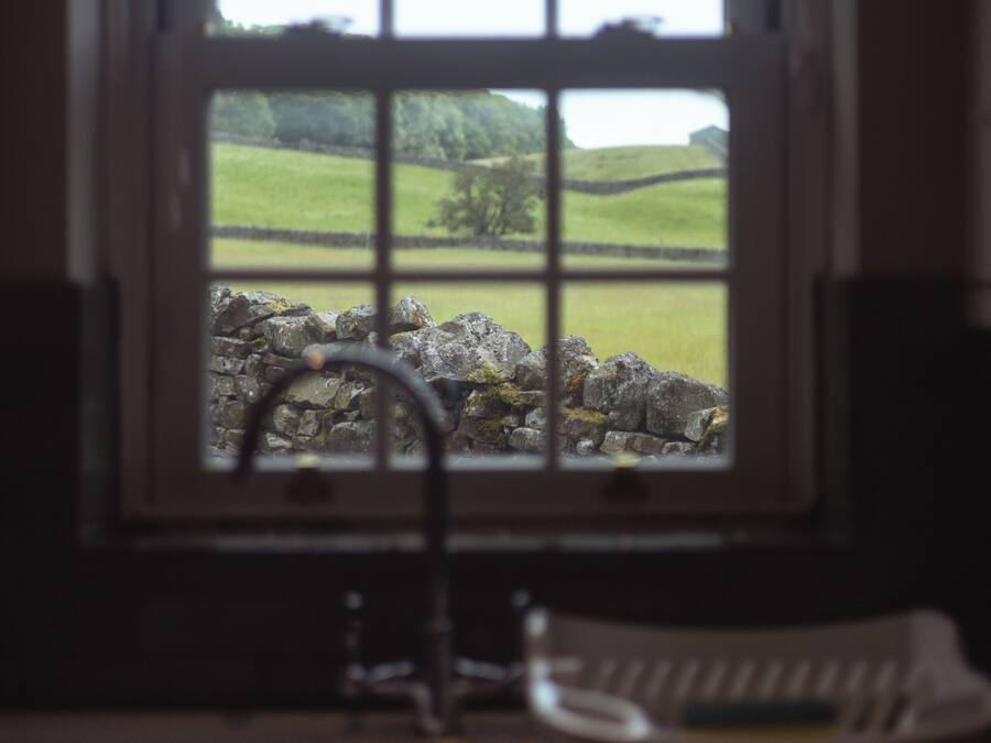 A window with a view of a stone wall and green fields.