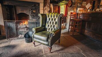A traditional pub interior with a leather armchair, a stone fireplace, and a bar area.