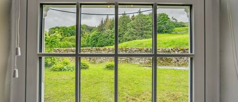 A window with a view of a green landscape, stone wall, and trees.