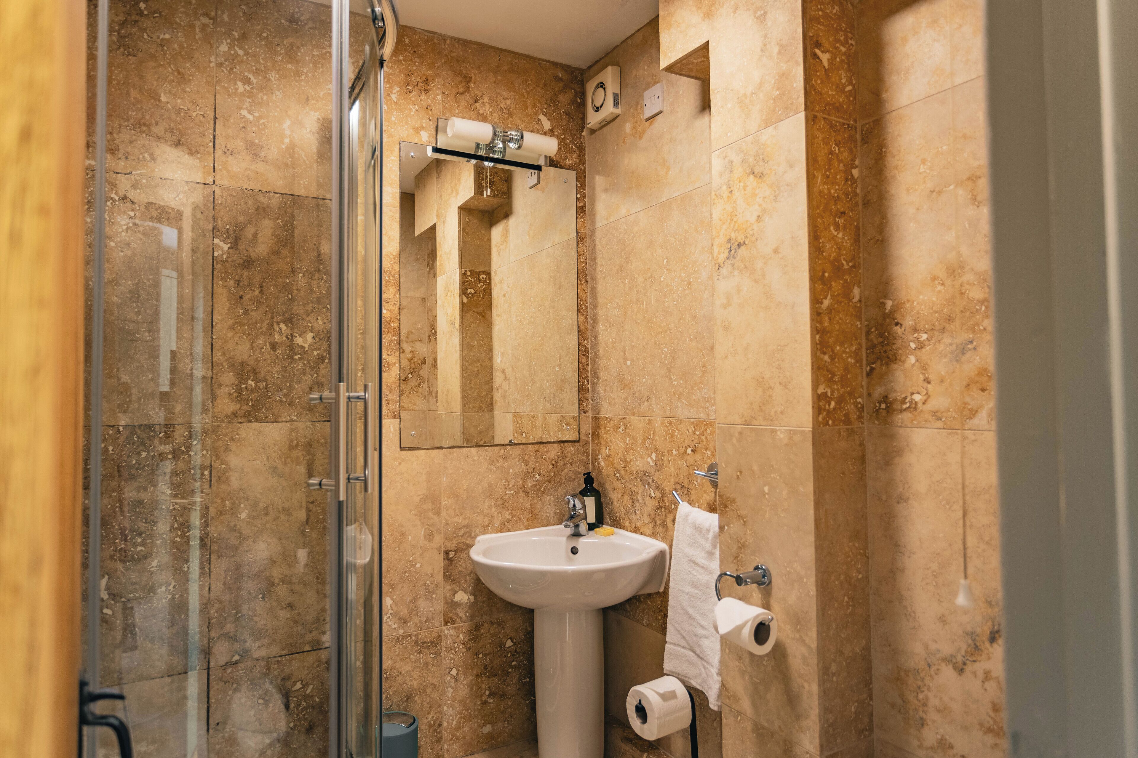 Een badkamer met een douchecabine van glas, een wastafel op een zuil en een spiegel.