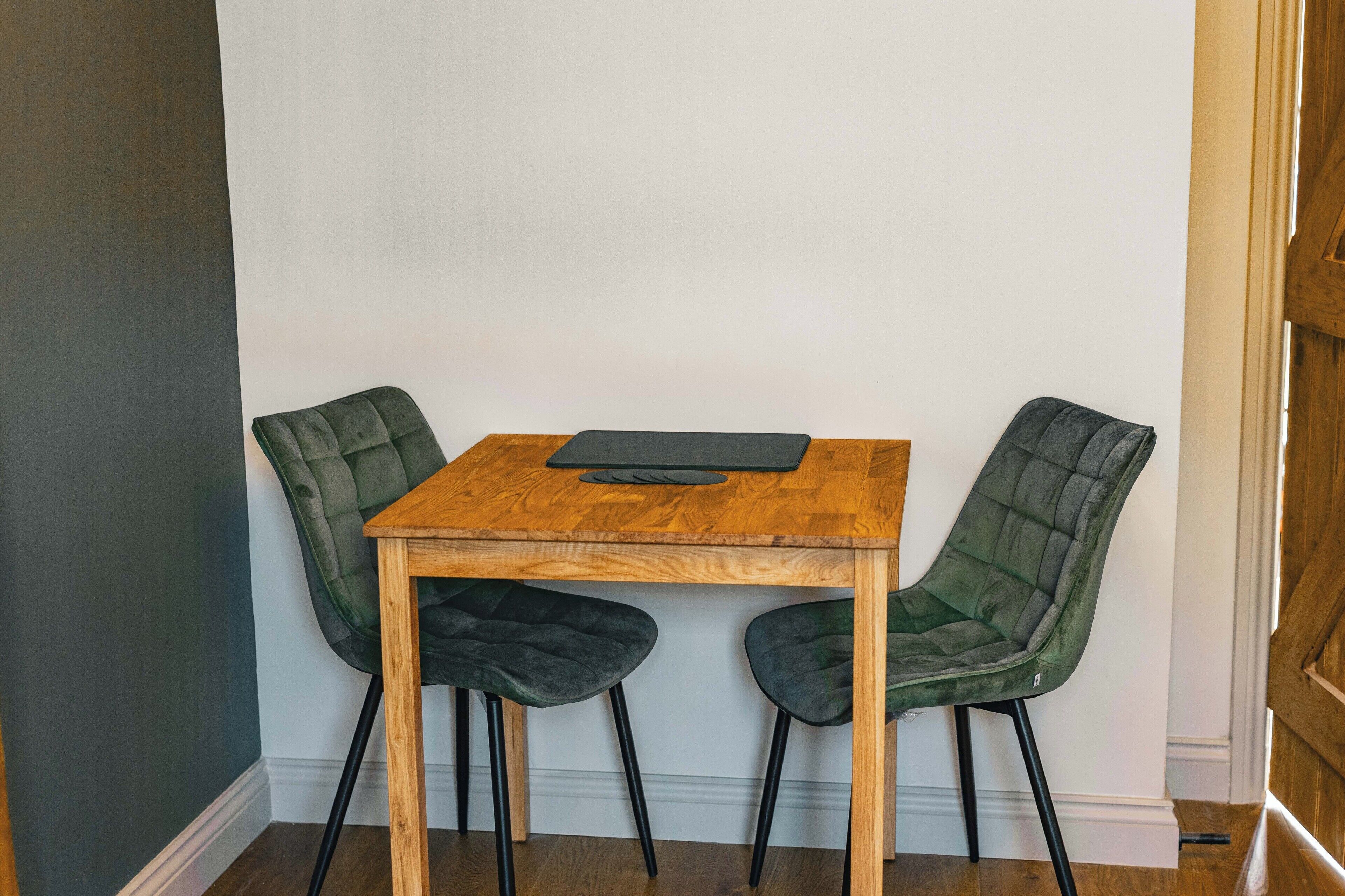 Een houten tafel met twee gestoffeerde stoelen, een zwarte placemat en een witte muur.