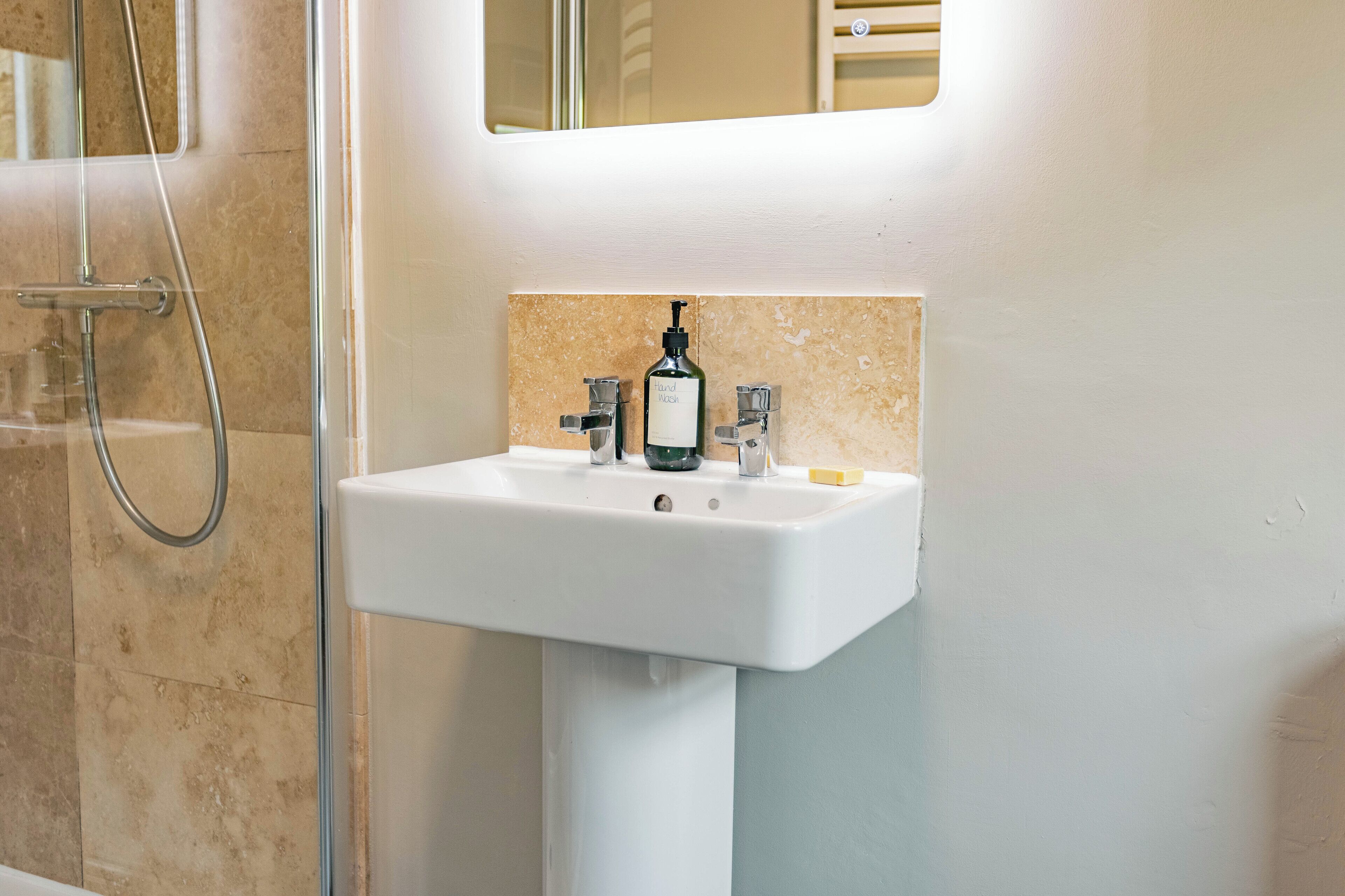 A bathroom with a white sink, a mirror above it, and a shower area to the left.
