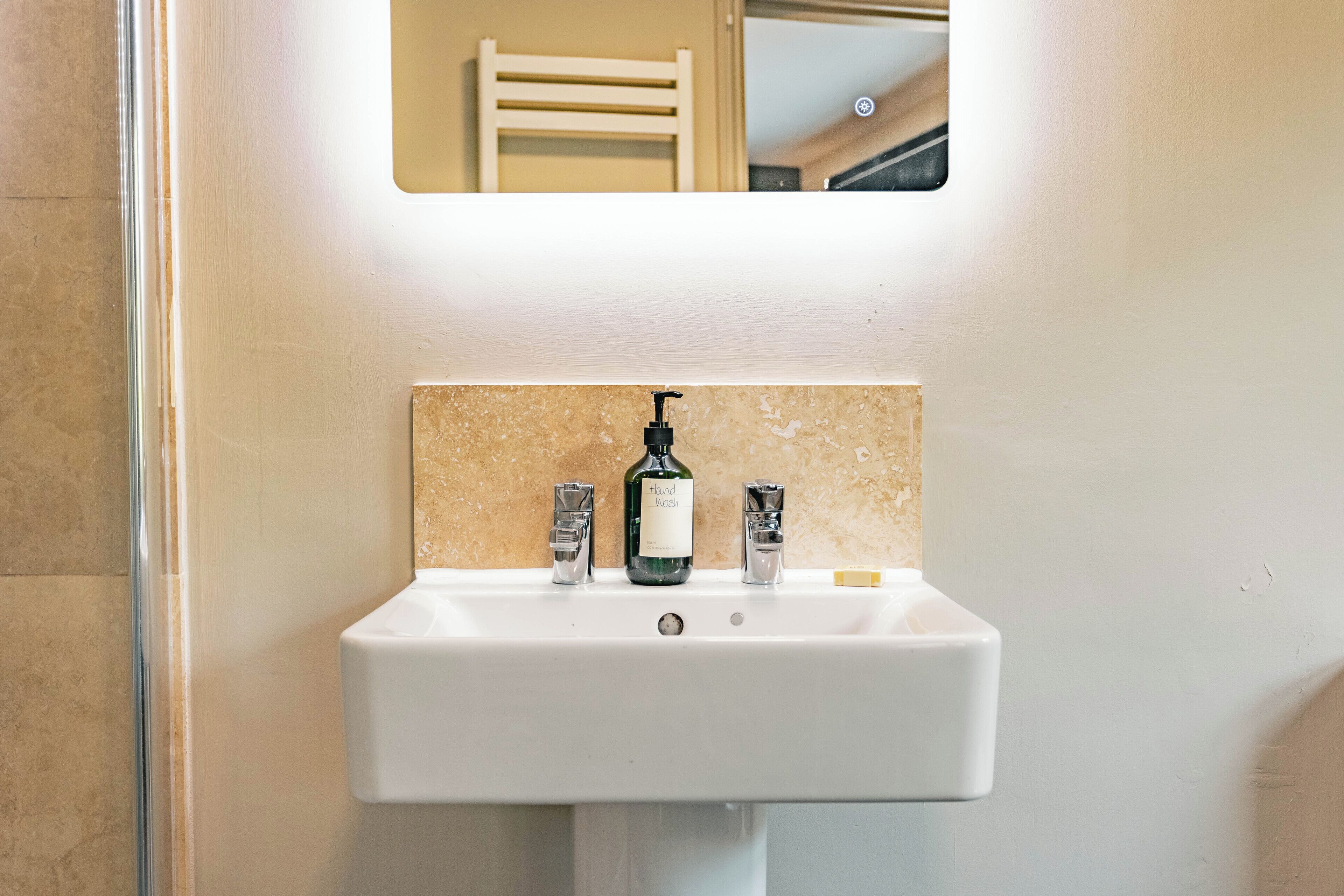 A bathroom sink with a mirror above it, a bottle of hand soap, and a soap dispenser.