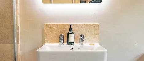 A bathroom sink with a mirror above it, a bottle of hand soap, and a soap dispenser.