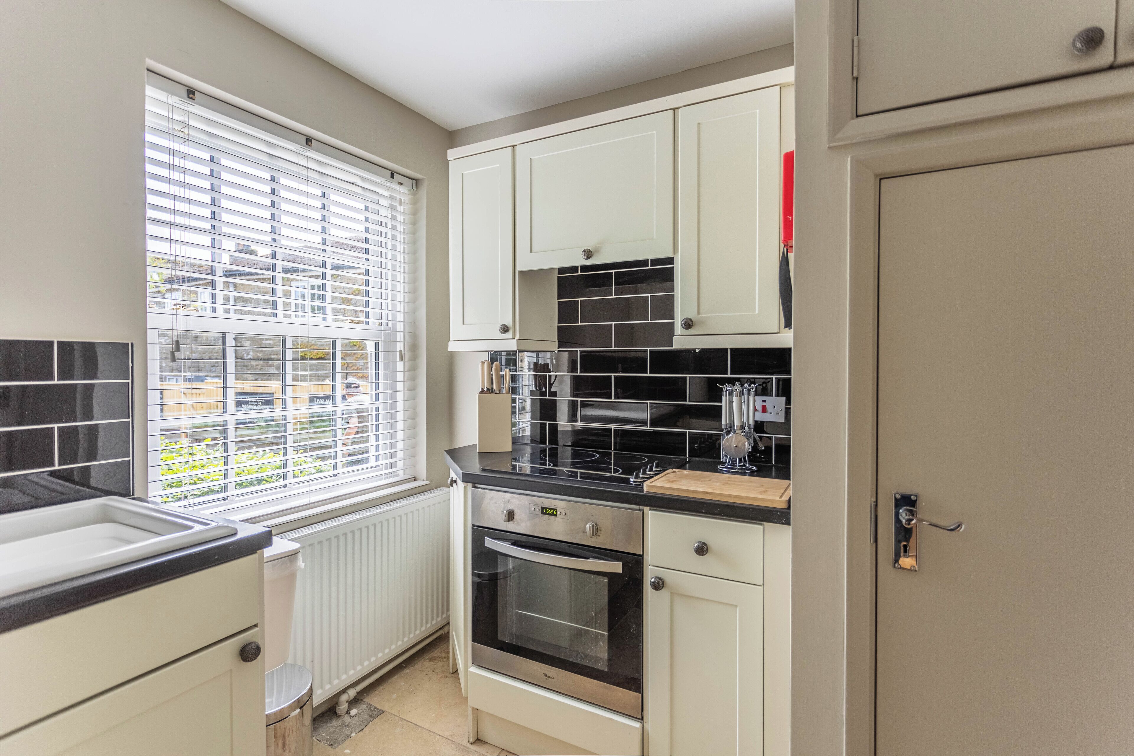 A compact kitchen with white cabinets, a black countertop, and a window with blinds.