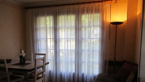 A room with a dining table, chairs, a sofa, and a lamp. - Gite les Lavandes, 4 Personnes (VALROS)
