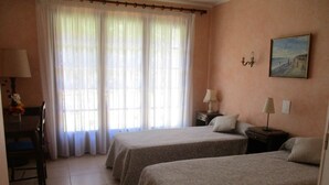 A hotel room with two beds, a desk, a chair, a lamp, and a painting on the wall. - Gite les Lavandes, 4 Personnes (VALROS)